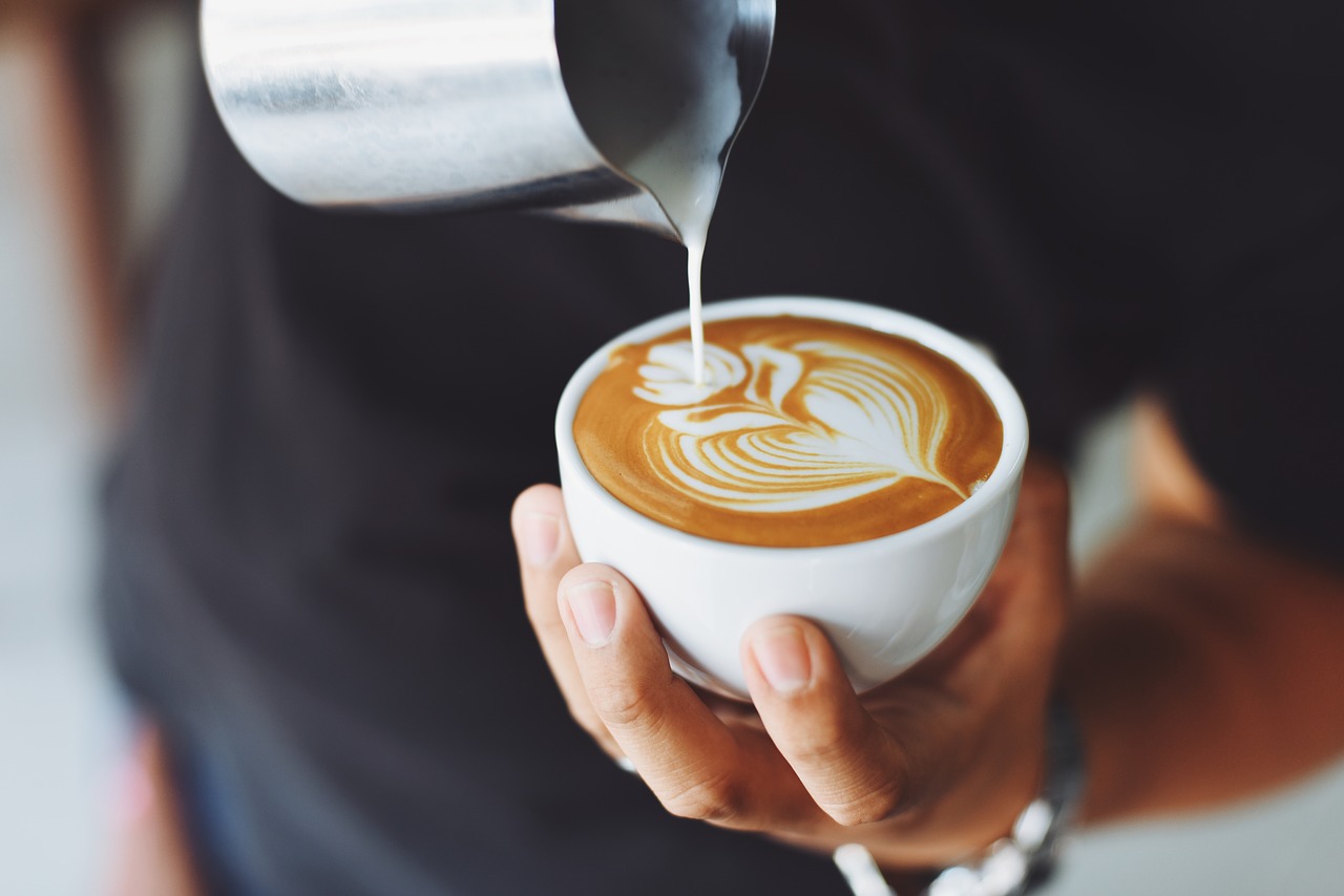 A person is pouring steamed milk into a cup of coffee, creating latte art.